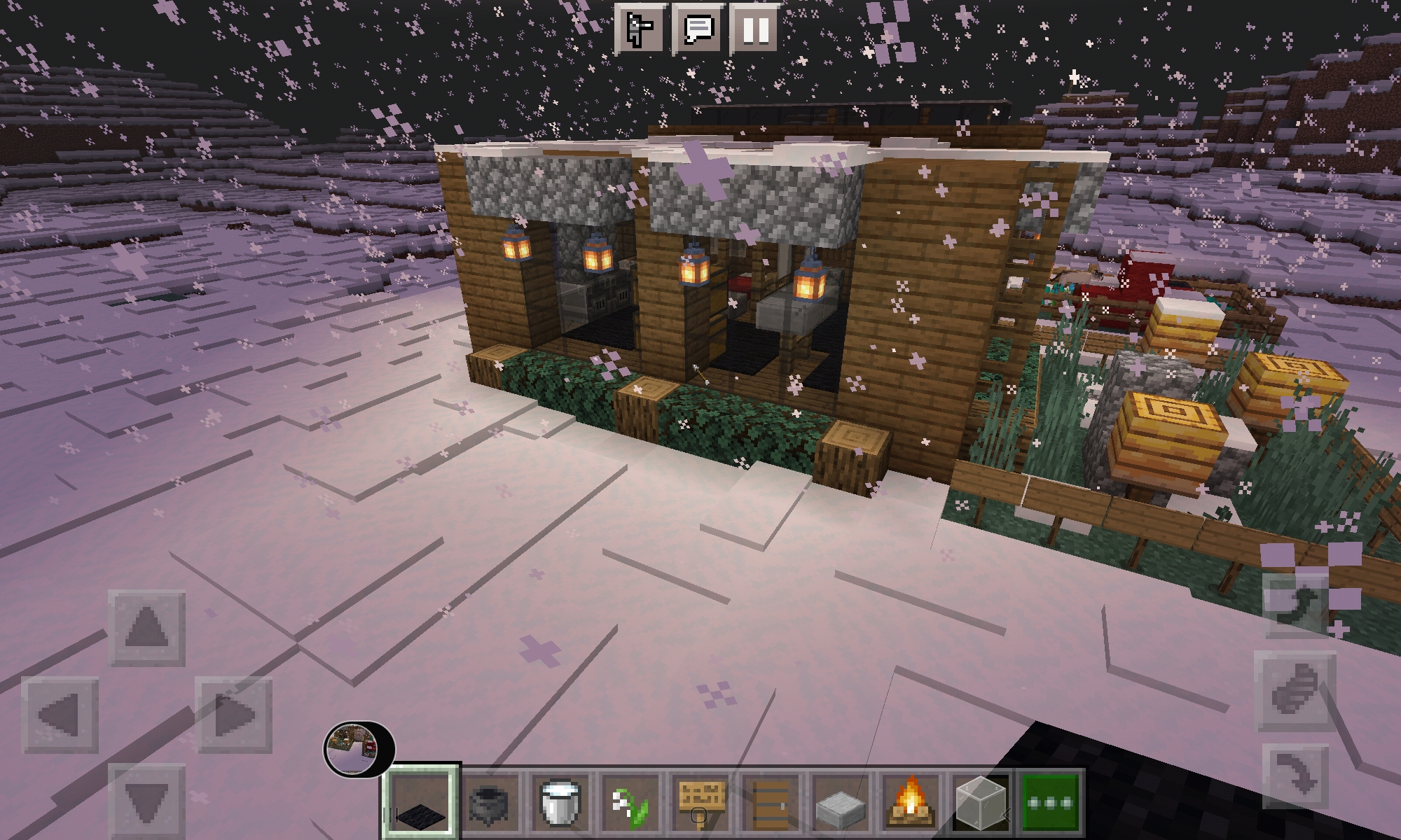 A small minecraft build of a modern cabin in the snow, featuring hanging lanterns and a small garden with bee hives.